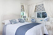 Bright bedroom with white and blue accents and floral window blinds