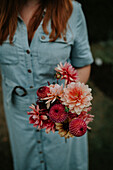 Woman in light blue dress with dahlia bouquet in garden