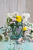 Bouquet of apple blossoms, lilacs and dandelions in a glass, with hearts made of string and sheet metal