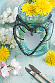 Dandelion (Taraxum) in hanger jar with hearts made of string and tin, sprigs of lilac blossom (Syringa) and apple blossom