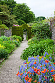 Gravel path through flowering garden with hedge arch and stone walls