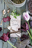 Arrangement mit Silberbesteck, Tulpen (Tulipa) und Osterei, Osterkarte und mit Namen beschriftetes Blütenblatt