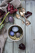 Arrangement mit Silberbesteck, Tulpen (Tulipa) und Ostereiern, gefärbt mit Rotkohl und Rote Bete, mit Namen beschriftetes Blütenblatt