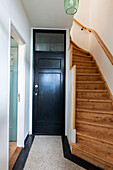 Narrow hallway with wooden staircase and black door