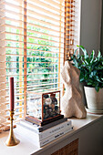 Pile of books and decoration on windowsill in front of wooden blinds