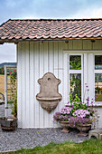 Wall fountain on a white garden shed, floral decoration