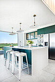 Modern kitchen with kitchen island, white bar stools and green-blue cabinets