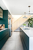 Modern kitchen with green-blue cabinets and kitchen island, a staircase in the background