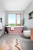 Modern bathroom with pink freestanding bathtub and large window