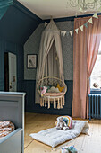 Children's room with hanging chair and canopy, wooden floor and decorative cushions