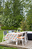 Gedeckter Holztisch mit Stühlen und gemusterter Tischdecke auf Holzterrasse im Garten