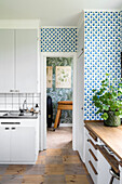 Retro-inspired kitchen with blue and white patterned wallpaper and wooden floor with chequerboard pattern