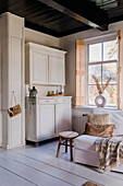 Rustic living room with white wooden cabinet and white armchair with blanket and cushions