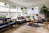 Bright living room with light grey corner sofa, round wooden coffee tables and indoor plants