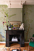 Fireplace with dark wooden frame in front of wallpaper with nature motif