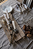Rustikaler Holztisch mit Kerzenständern, Geschirr und Tannenzapfen