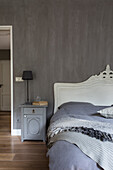 Schlafzimmer mit grauer Wand, weißem Barock-Kopfteil und Nachttisch in Graunuance