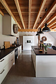 Modern kitchen with cooking island, wooden beamed ceiling and pendant lights