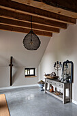 Attic with wooden beamed ceiling, concrete floor and vintage-style sideboard