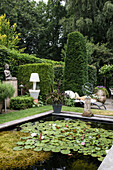 Well-tended garden with water lily pond, high hedges and Buddha statue