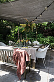 Laid garden table with fresh cut flowers under a sunshade with fairy lights