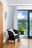 Black wicker armchair next to sliding glass door with view of green hills