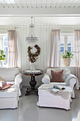 Bright living room with white armchairs, cushions, blanket, furs and crystal chandelier