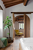 Bedroom with wooden floor, pouf and large plant, view into the neighbouring room