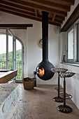 Hanging fireplace in rustic living area with wooden beamed ceiling and metal bar stools