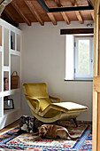 Yellow armchair with footrest in room with wooden beamed ceiling, two dogs on patterned carpet