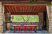 Covered outdoor dining area with stone pillars and red chairs