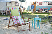 Deckchair in the sand in front of camper with small blue side table