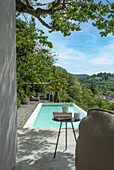 Terrasse mit Swimmingpool, Blick auf grüne Hügel, Tisch mit Tassen und Büchern