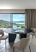 Round dining table with chairs in front of panoramic window with lake view