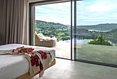 Schlafzimmer mit Panoramafenster und Aussicht auf Hügellandschaft und See