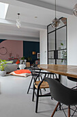 Open-plan living and dining room with wooden table, black chairs and industrial-look glass door