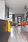 Open-plan living room with orange-colored chairs and light wood-look flooring