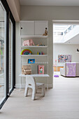 Play corner with white shelves, children's chair and toys next to large windows