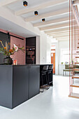 Modern kitchen in black and white with pink tiled wall and counter with bar stools