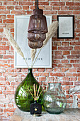 Green glass vases with pampas grass and wall posters in front of brick wall