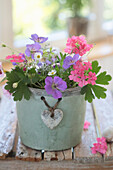 Bouquets of cranesbill, verbena and daisies in a clay pot with a heart decoration