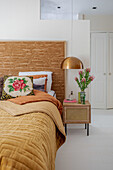 Bedroom with relief headboard, ochre-colored bedspread and flower arrangement on bedside table