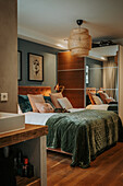 Bedroom with green velvet bedding, mirrored wardrobe and rattan lamp