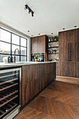 Modern kitchen with dark wooden cupboards, large window and herringbone parquet flooring