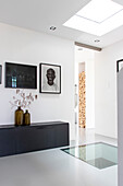 Modern hallway with glass floor, black sideboard and art portraits on the wall