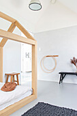 Bright children's room with wooden bed in the shape of a house, grey carpet and hula hoops on the wall