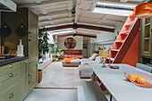 Open-plan green eat-in kitchen with dining area and red staircase to skylight