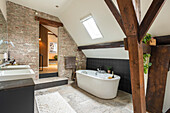 Free-standing bathtub in modern bathroom with brick walls and sloping roof