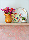 Flowers in yellow ceramic jug in front of decorated plates on wooden shelf