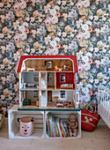 Doll's house on wooden crates in front of floral wallpaper in the nursery